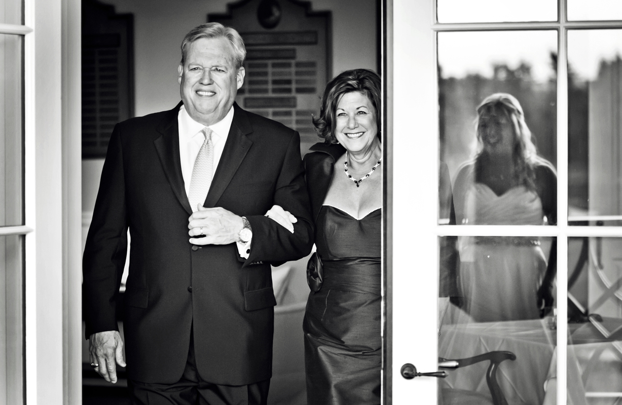 A black and white photo of a smiling couple dressed formally indoors.