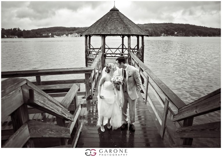 A bride and groom walk hand in hand on a dock by a lake.