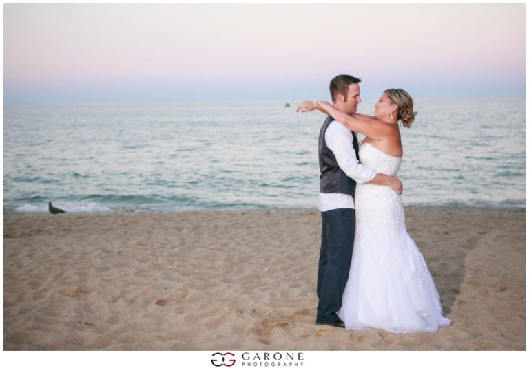 Bride and groom embracing on a beach at sunset.