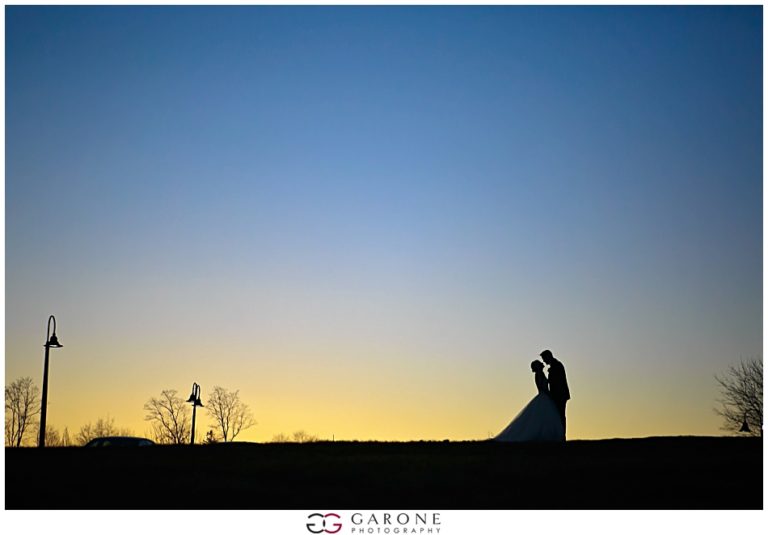Silhouetted couple embraces at sunset on a hilltop.