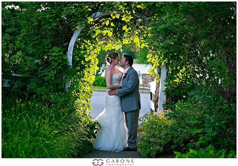 Bride and groom share a kiss under a lush green archway.