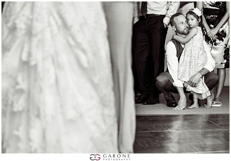A young girl clings to a man during a formal event, with a blurred figure in the foreground.
