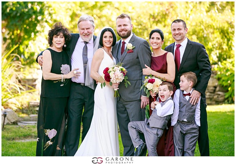 A joyful wedding group photo with the bride, groom, and family outdoors.