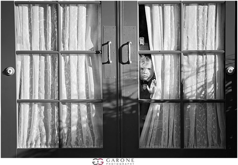 A child peeks through a partially open window behind curtains.