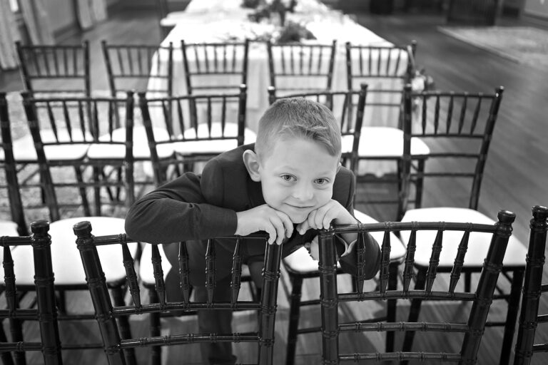 Young boy leaning on wooden chairs outdoors, smiling at the camera.