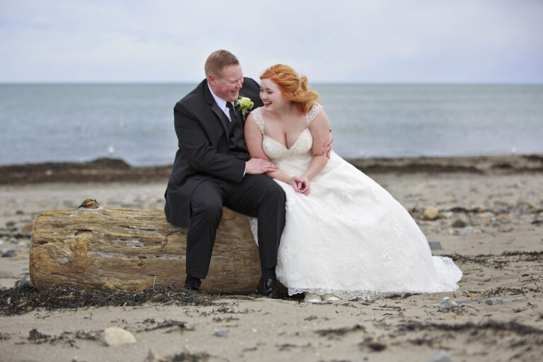 Newlywed couple sharing a joyful moment on a rocky beach.